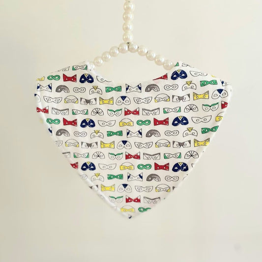 A baby dribble bib with colourful superhero masks, hanging from a pearl string against a plain background.